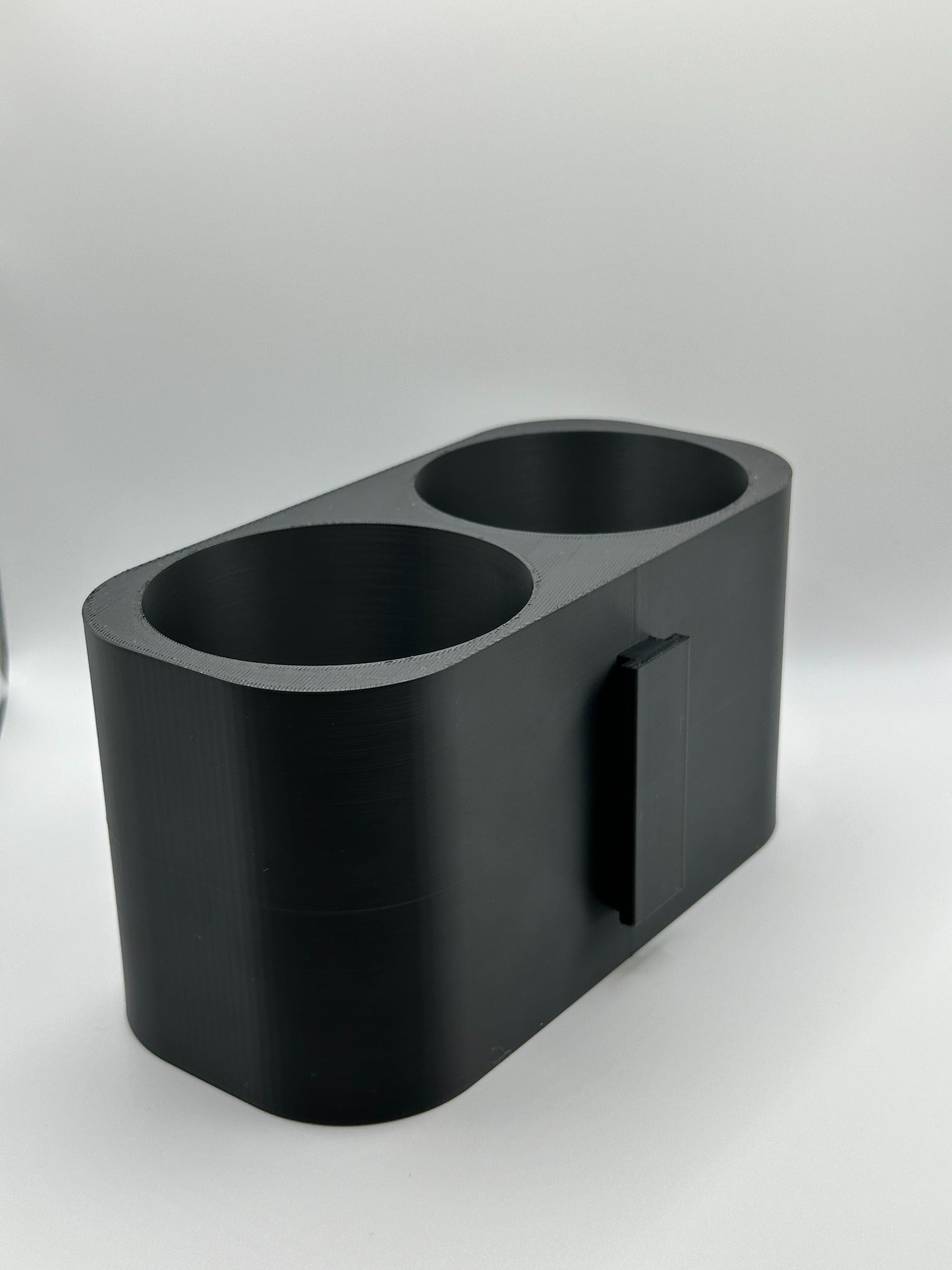 Zijaanzicht van een 3D-geprinte dubbele bekerhouder met een matzwarte afwerking.
